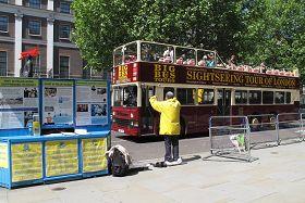 倫敦觀光車上，導遊向遊客介紹法輪功24小時傳真相活動。後面為中領館。